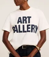 Remera blanca de algodón con cuello redondo y mangas cortas. Estampa frontal con la frase "ART GALLERY" en letras mayúsculas azules.