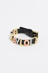 Pulsera de cuero negro con letras metálicas tricolor con el nombre de la marca. Cierre con hebilla metálica dorada y logo grabado.