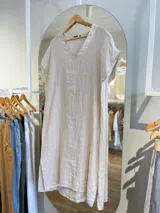 Vestido midi de lino color beige, corte recto, con escote en V y mangas cortas. Presenta aberturas laterales en el ruedo.