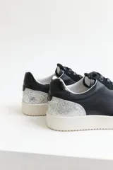 Zapatillas urbanas de cuero negro con cordones negros y suela blanca.
