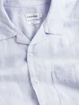Camisa celeste de manga corta con cuello cubano, cierre frontal con botones y bolsillo de parche en el pecho.