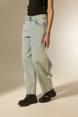 Pantalón de jean negro de corte ancho y tiro bajo, con detalles de tachas metálicas en los bolsillos delanteros y a lo largo de las costuras laterales.