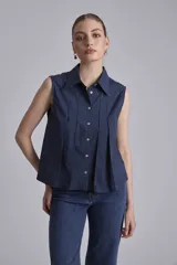 Camisa azul marino sin mangas con cuello clásico, abotonada al frente y detalle de plisados verticales en el pecho.