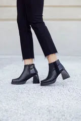 Botinetas negras de cuero con caña baja, cierre lateral y detalle de cuero texturizado en el talón. Taco geométrico y punta cuadrada.