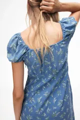 Vestido largo de lino y viscosa color celeste con estampado de flores blancas. Tiene mangas cortas abullonadas, escote corazón con tiras finas, copas preformadas con frunces, elástico en escote, hombros, mangas y cintura, cierre lateral oculto y tajo pronunciado en un lado.
