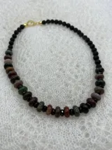 Collar corto de cuentas de piedra natural en tonos marrones, verdes y negros, con cierre de gancho dorado.