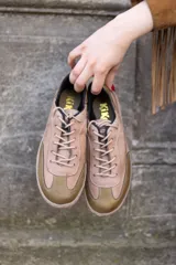 Zapatillas bajas de cuero color beige con puntera y talón en verde oliva. Cordones finos color beige y suela de goma color caramelo con costuras blancas.
