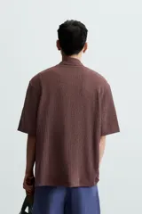 Camisa de manga corta con cuello bowling y calce relajado. Presenta un tejido con textura estructurada y efecto lavado, con cierre frontal de botones al tono.