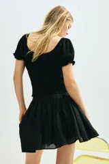 Blusa negra con escote cuadrado, mangas cortas abullonadas con elástico en hombros y puños, cintura fruncida y abertura con cordón para ajustar en el delantero.