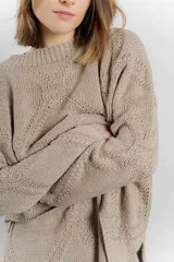 Sweater color arena de tejido geométrico con calce relajado, hombros caídos y terminaciones suaves.