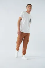 Pantalón cargo color marrón con corte slim, elástico en cintura y cordón ajustable, bolsillos cargo con botones y puños elásticos. Confeccionado en algodón y spandex.