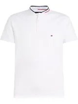 Chomba blanca de corte slim con cuello mao, tapeta de tres botones y logo de Tommy Hilfiger bordado en el pecho. El cuello presenta una banda con los colores característicos de la marca: azul marino, blanco y rojo.