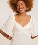 Vestido corto evasê de viscolino color crudo, con escote en V, mangas cortas amplias, recorte cut-out en los laterales de la cintura y volado en el ruedo.