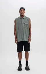 Camisa sin mangas color verde militar, con cuello, cierre frontal de botones y un bolsillo de parche con tapa en el pecho izquierdo. Presenta un calce oversize.