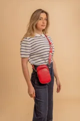 Bandolera pequeña tipo 'phone bag' de símil cuero color rosado pálido, con cierre de cremallera y correa ancha de tela con diseño de chevron en tonos claros.