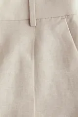 Short color beige de tiro alto con pliegues delanteros, bolsillos al bies y cierre frontal con botón y corchete ocultos.