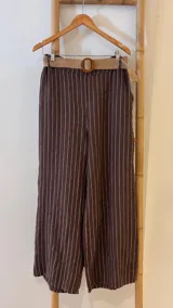 Pantalón de lino azul marino con rayas verticales blancas, corte palazzo, cintura alta con elástico y cinturón de raffia con hebilla redonda.