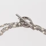 Pulsera plateada de tres hilos con cuentas blancas y cierre de gancho.