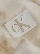 Buzo Calvin Klein de algodón con capucha y estampado tie dye en tonos beige y blanco. Tiene puños y dobladillo de punto canalé y logo CK estampado en el pecho.