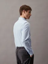 Camisa celeste de popelín de algodón elástico, corte slim, manga larga y cierre frontal con botones.