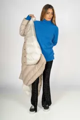 Campera puffer larga color beige, con cuello alto y cierre frontal con botones a presión. Tiene bolsillos laterales y un parche con el logo de la marca en la manga izquierda.