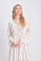 Vestido corto blanco con estampado de paneles geométricos dorados, escote en V con lazo ajustable y mangas largas acampanadas.