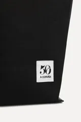 Bolso tipo tote confeccionado en algodón color negro, con doble asa y detalle de parche con el logo "50" y la leyenda "A Coruña".