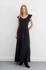 Vestido largo negro sin mangas, con escote redondo, espalda baja y volados en el escote. Ajuste en la cintura con cordón y terminaciones metálicas.