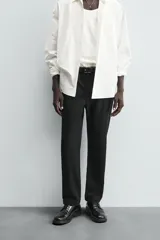 Pantalón chino negro de corte relajado (relaxed fit) con tiro medio, confeccionado en algodón con elasticidad. Presenta bolsillos delanteros y bolsillos traseros de vivo, con cierre frontal de cremallera y botón.