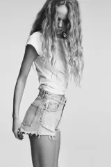 Short de jean de tiro alto, color celeste claro desgastado, con roturas grandes y deshilachado en el bajo. Presenta cinco bolsillos y cierre frontal con botón metálico.