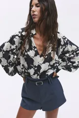 Blusa oversized con cuello elevado fruncido, abertura en V adelante y bajo recto. Mangas globo largas de corte raglán con abertura y botón en los puños.