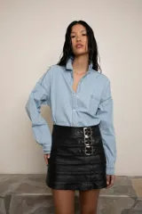 Minifalda negra de cuero con costuras horizontales y tres hebillas metálicas plateadas en el lateral.