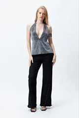 Pantalón negro de denim con calce wide leg y ruedo desflecado. Presenta tachas metálicas a lo largo de los laterales.