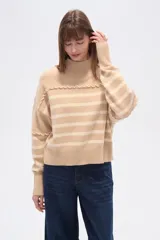 Sweater beige con rayas horizontales negras, cuello alto y corte holgado.