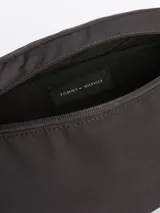 Riñonera negra de poliéster con correa ajustable, cierre de cremallera, bolsillo interior con cremallera, panel trasero acolchado y logo engomado de Tommy Hilfiger en el frente.