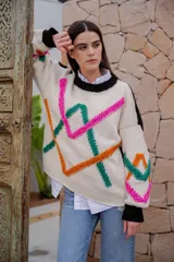 Sweater de punto color crudo con cuello redondo negro y bordados decorativos en forma geométrica en colores fucsia, verde y naranja. Tiene mangas largas con puños negros.
