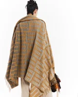 Manta de tejido grueso con flecos en los bordes, color mostaza y gris, con diseño de monograma repetitivo.