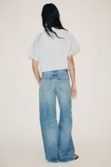 Camisa blanca corta con rayas verticales celestes, cuello solapa y mangas cortas con dobladillo. Tiene un bolsillo de parche en el pecho y cierre frontal con botones ocultos.