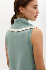 Chaleco de punto sin mangas, color azul marino, con cuello y frente adornados con volados en contraste de color blanco o crudo.