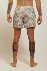 Short de baño para hombre, tiro medio, con estampado tropical en tonos rosados, verdes y blancos. Posee cintura elástica con cordón de ajuste trenzado y bolsillos laterales.