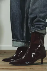 Botín color bordó con efecto acharolado, caña baja, tacón kitten de 4 cm y punta fina. Cierre mediante cremallera lateral.