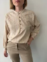 Blusa color beige con estampado a cuadros, cuello mao, mangas largas abullonadas y cierre frontal con botones.