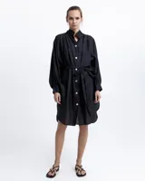 Vestido camisero negro de ramio con cuello mao, mangas largas abullonadas, cierre frontal con botones blancos y lazo a la cintura.