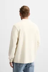 Polo color crema de manga larga con cuello solapa y cierre frontal de botonadura.