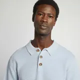 Remera tipo polo celeste de punto con cuello clásico y tres botones marrones.