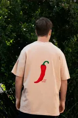 Remera color crema de manga corta con estampado de un ají rojo y la frase "Just Chilli" en la espalda.
