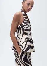 Chaleco con estampado de cebra en blanco, negro y beige, con cuello halter y corte peplum. Presenta pinzas en la cintura, panel elástico en la parte posterior y cierre de botones en la parte delantera.