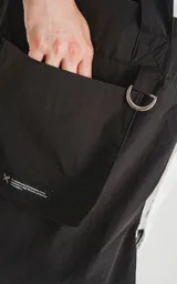Bolso tote negro de tela técnica de microfibra de secado rápido, con espacio principal para llevar pertenencias. Cuenta con un elástico ajustable con tanca y contiene dos bolsillos, uno interno con cierre y otro externo con velcro.