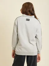 Polo manga larga gris con cuello clásico, cierre de botones parcial, logo de la marca estampado en el pecho y dos rayas negras en cada manga.