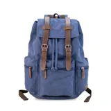 Mochila de tela canvas color verde oliva con tapa y detalles en símil cuero marrón. Cierre superior marinero, bolsillos internos, externos frontal, laterales y trasero con cierre. Asas rígidas, correas ajustables y espacio para laptop de 15".